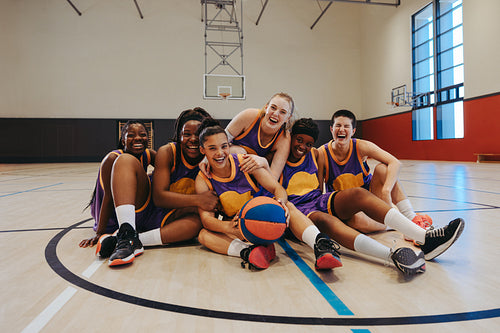 Joyful young women's basketball team celebrating together on indoor court