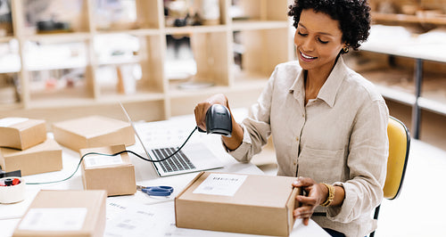 Cheerful female entrepreneur scanning the barcode of a package box in a warehouse