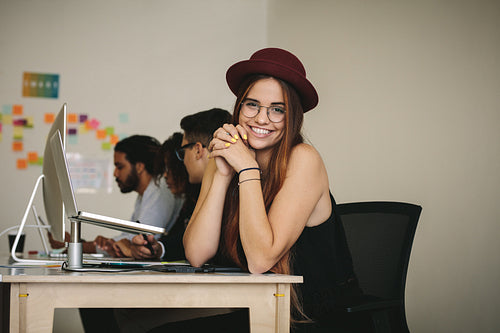 Smiling businesswoman in hat and eyeglasses sitting at her desk in office