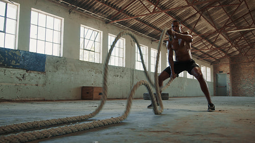 Fitness man doing battle rope workout in gym