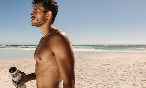 Man standing at the beach drinking water after workout