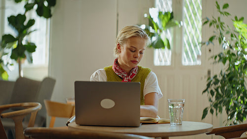 Woman works on a laptop and writes notes at a cafe table