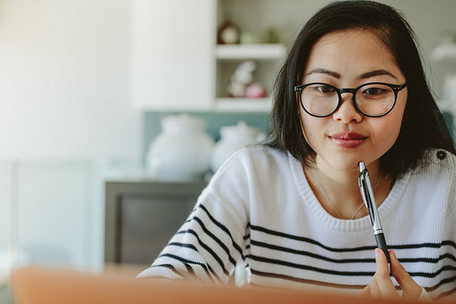 Woman using laptop with a pen in hand
