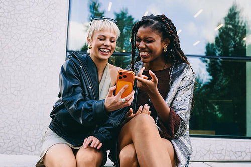 Friends share a smartphone and laugh outdoors