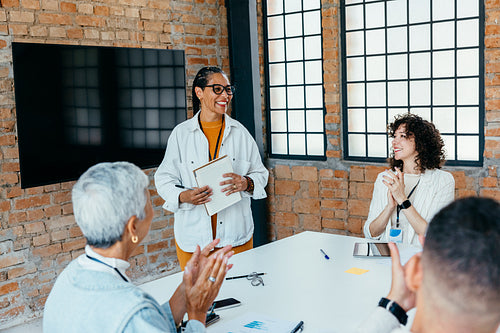 Pleased businesswoman smiles during successful team meeting as colleagues clap in a sleek and modern workplace setting