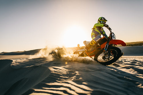 Motocross driver in action on sand dunes