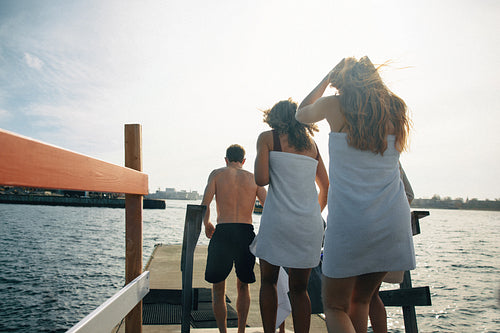 Friends walking on dock for a winter ocean swim at sunny harbor