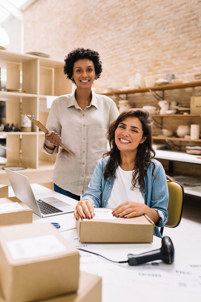 Successful online store owners smiling at the camera in their warehouse