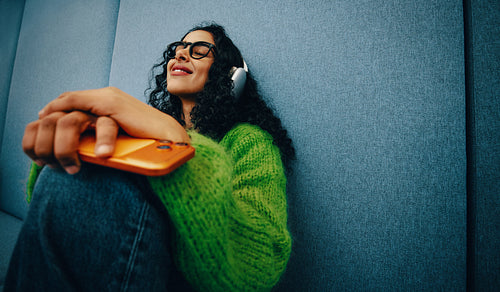 Young woman relaxing with smartphone in study lounge wearing headphones