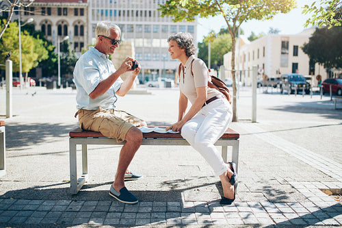 Senior tourist sitting on a bench looking pictures on camera