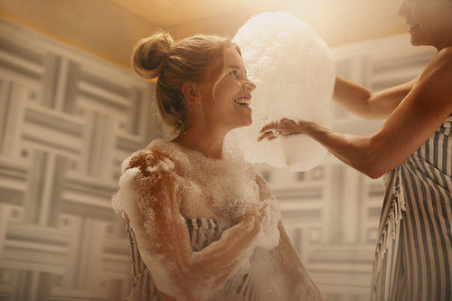 Mature woman and younger woman enjoying a bubble bath in a hammam with lots of soap and laughter