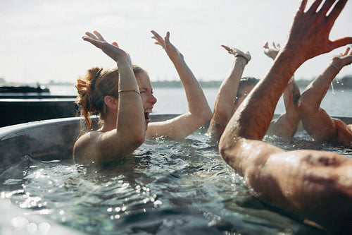 Joyful group high-fiving in outdoor hot tub by the water