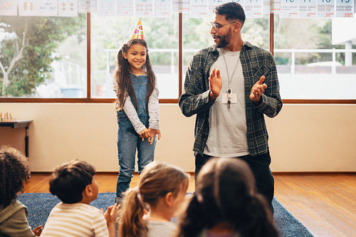 Primary school birthday celebration. Girl wearing a cone hat and standing in front of her class on her birthday