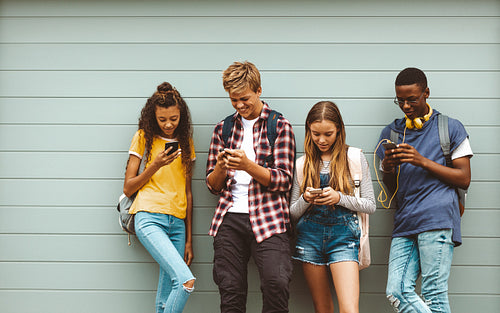 Teenage boys and girls using cell phones standing outdoors
