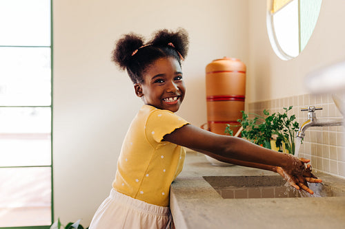 Happy afro-brazilian girl washing hands in kitchen sink