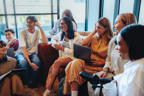 Multicultural group of students enjoying a lively school discussion in a modern classroom setting with laptops and notebooks