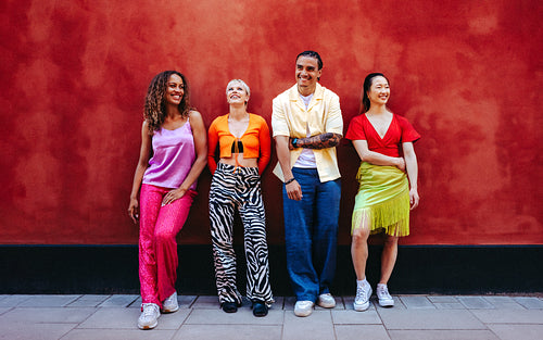 Happy friends stand together as a group against a red studio wall