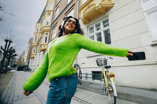 On a city walk, the woman smiles with podcast audio playing on her smartphone