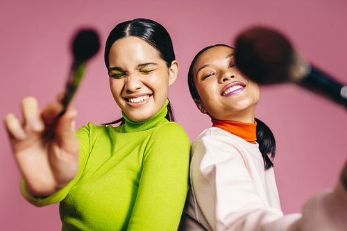 Glamour in Generation Z: Two females holding makeup brushes and having fun in a studio
