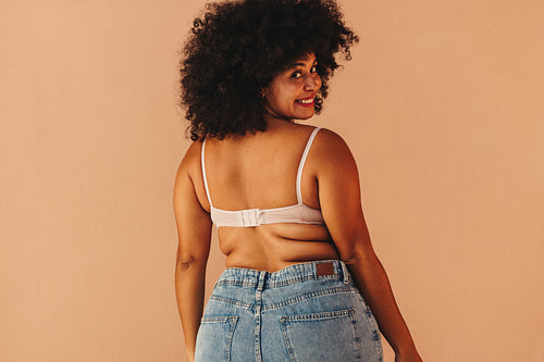 Rearview of a beautiful young woman wearing a bra and jeans in a studio