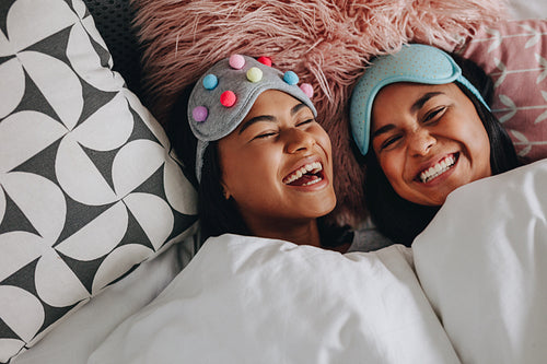 Happy girl friends laughing lying on bed