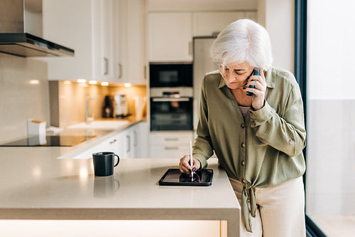 Senior woman making notes during a phone call at home
