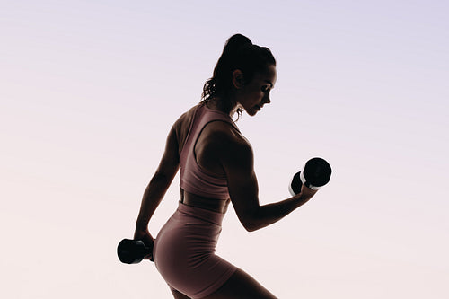 Silhouette of a lean and toned woman exercising with dumbbells in a fitness studio