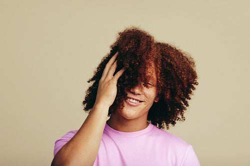 Happy youthful man embracing his curly ginger hair in a studio