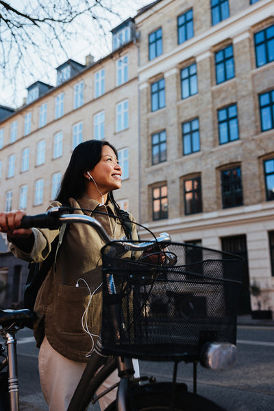 Smiling woman with bicycle in city listening to music