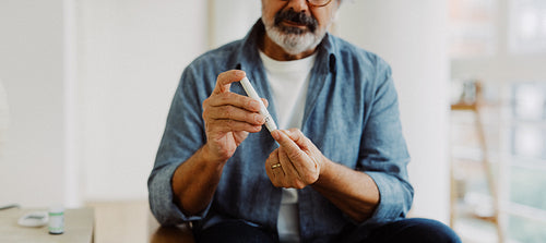 Senior man tests blood glucose at home with lancet