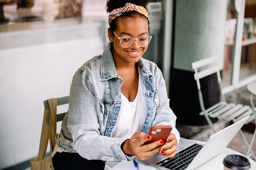Cheerful woman browsing social networks with her phone at a cozy cafe