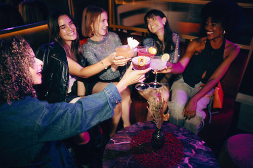 Group of friends toasting cocktails in a lively and stylish nightlife setting