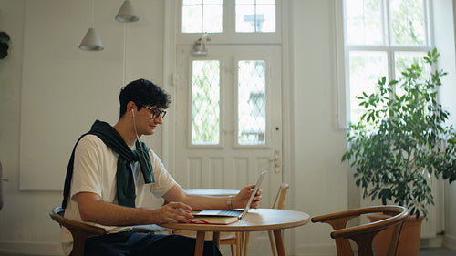 Man joins a laptop video call while taking notes at a cafe table