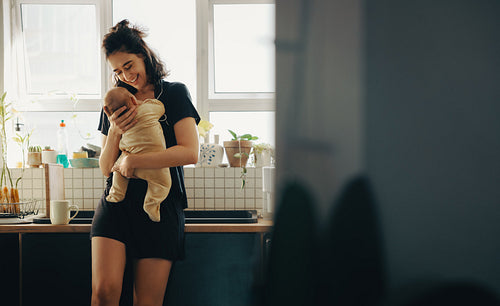 Mother joyfully holds baby in sunny kitchen.