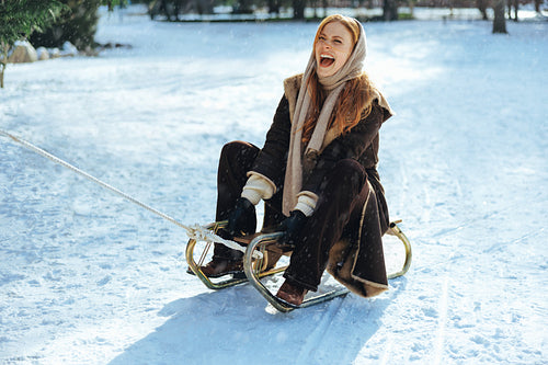 Woman laughs while sledding in snow with friends