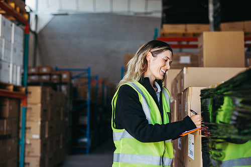 Happy warehouse manager writing on a clipboard in a logistics centre