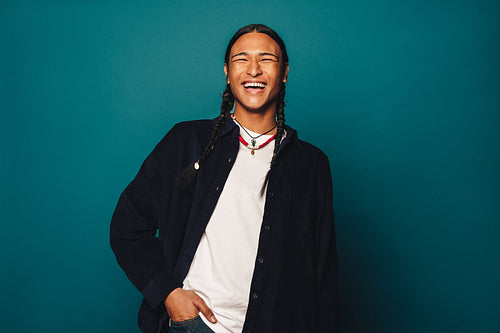 Confident native man with stylish braided hair and jewelry smiling on blue background