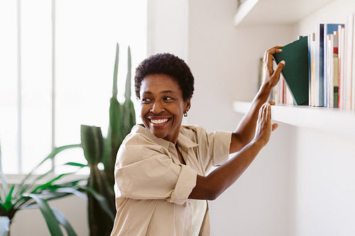 Woman smiling while choosing a book from her home library collection