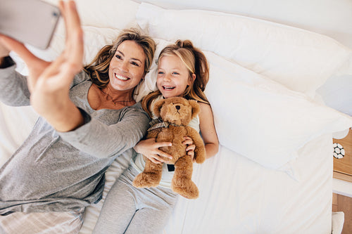 Young family taking selfie with smartphone in bed