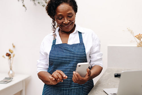Mature female entrepreneur using mobile phone in creative flower shop