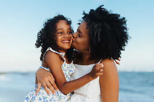Loving mother kissing her smiling daughter on the beach