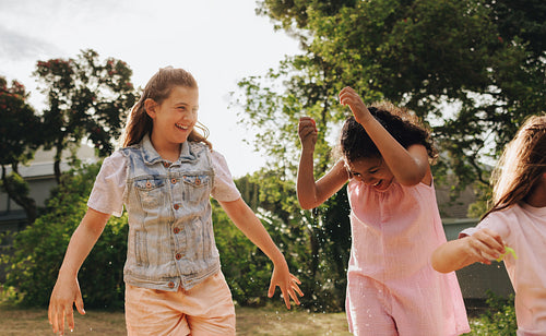 Three joyful children playing outside with water during a sunny day
