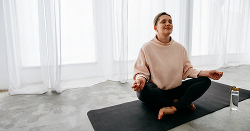 Meditation shapes the yoga routine as a woman sits at home on a mat