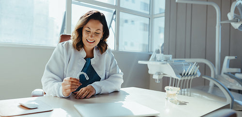 Female dentist examines clear aligner at desk in dental clinic