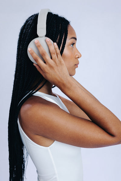 Stylish woman with black braids listening to music on wireless headphones
