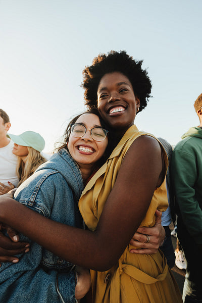 Two women smiling and embracing at a lively outdoor protest or rally