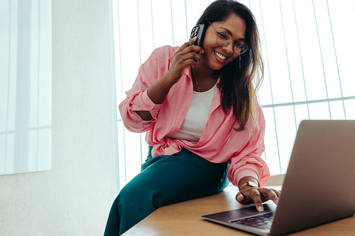 Indian female entrepreneur taking notes on a laptop while on a phone call