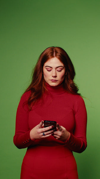 Young woman in red dress checks her phone against a green screen