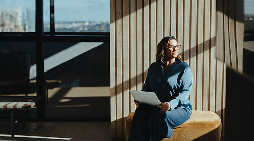 Thoughtful caucasian business woman with laptop by window in modern office