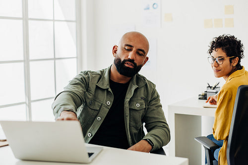 Software designer points to his laptop while talking to his colleague